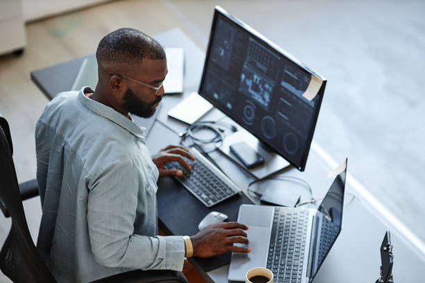 Minimal high angle view at African American software developer working with computers and data systems in office